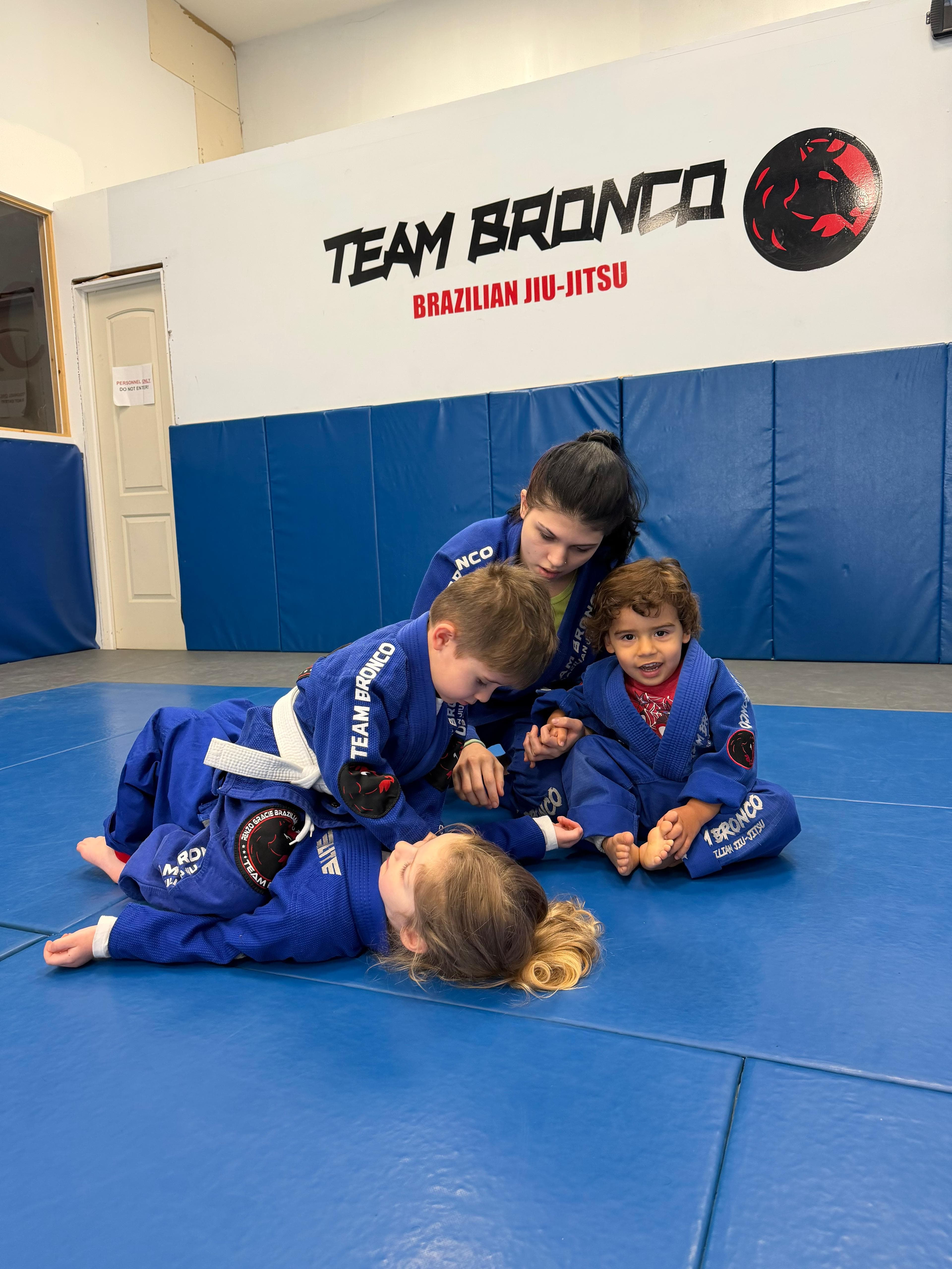 A coach guiding three young students through a technique on the mat at Renzo Gracie Garwood