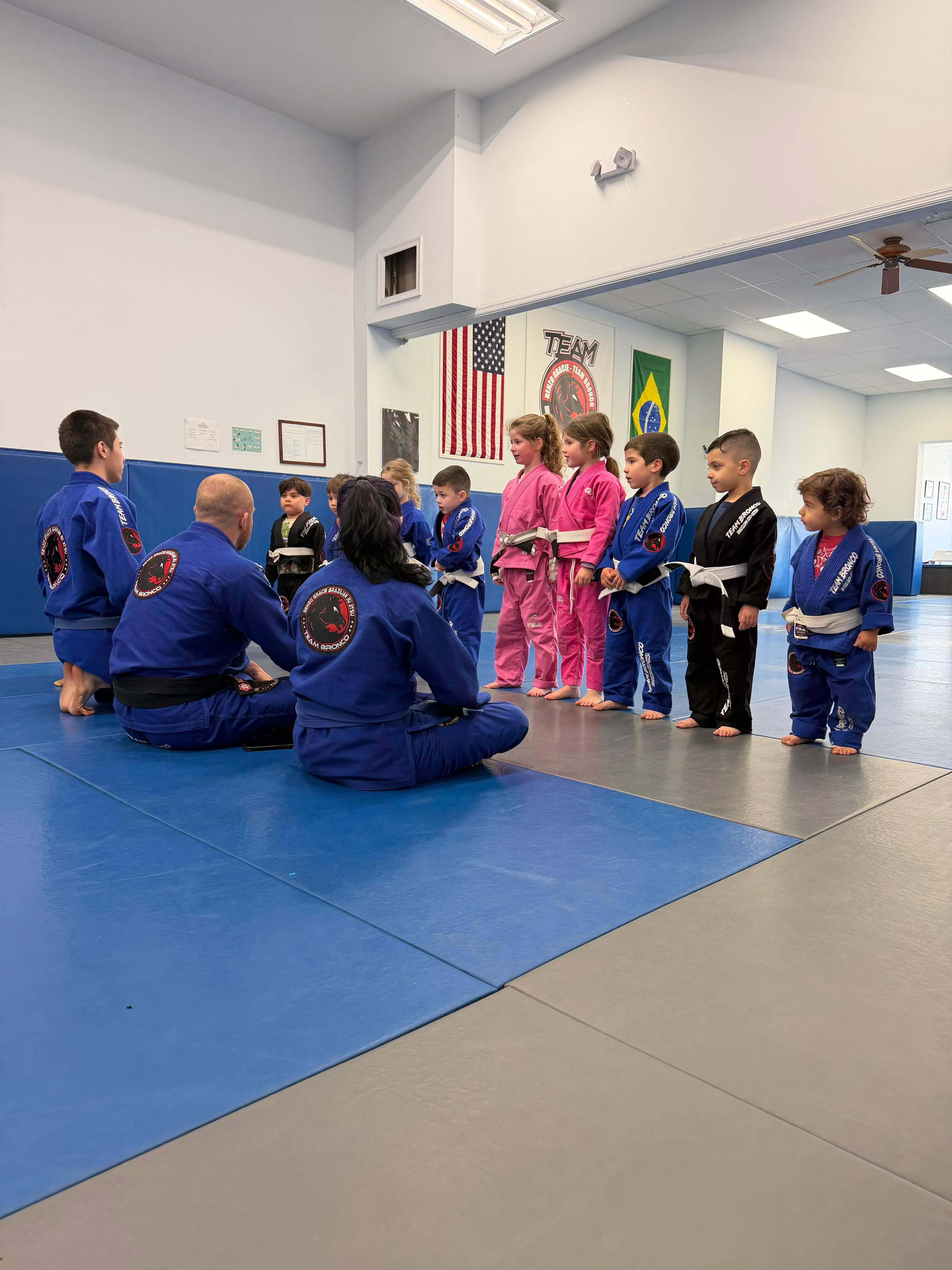 A kids Brazilian Jiu-Jitsu class lined up in front of their coaches on the mat